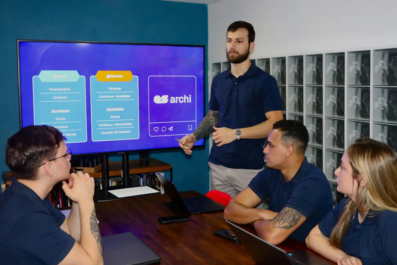 Equipe da Archi Soluções reunida em sala de reunião, discutindo estratégia de conteúdo e parcerias em frente a uma TV com o logo da empresa